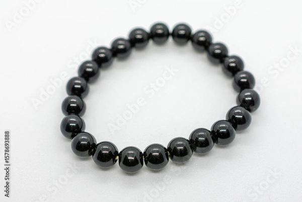Fototapeta Black bracelet with a shiny surface. The bracelet is made of small black beads. The beads are arranged in a circular pattern. The bracelet is made of a shiny material that reflects light.
