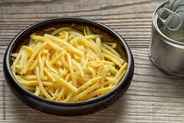 Fototapeta Canned bamboo shoots in bowl. Empty tin can on the side. An important ingredient in Asian cuisine. Rustic wooden table. 