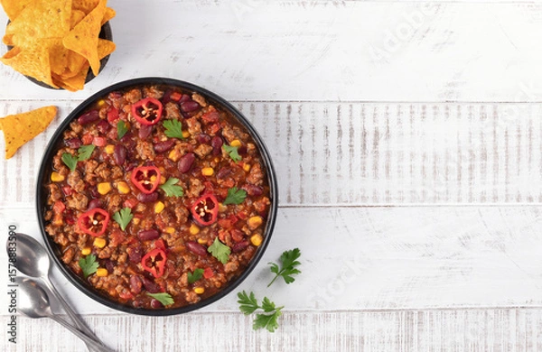 Fototapeta Bowl of meat mexican spicy stew with beans and corn chili con carne on white wooden background. Top view. Copy space.