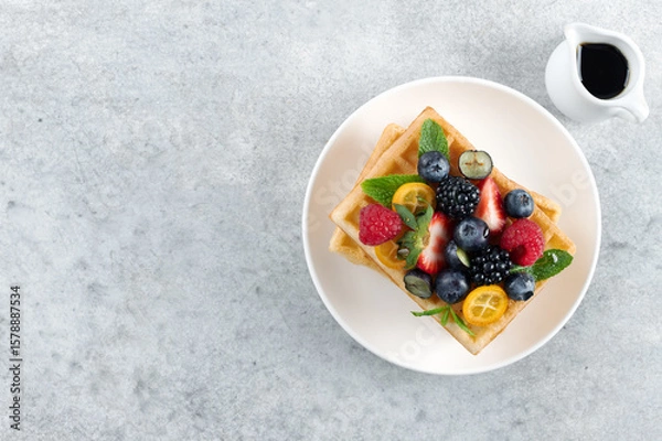Fototapeta Belgian waffles with fresh raspberries, blackberries and maple syrup on gray background. Top view.
