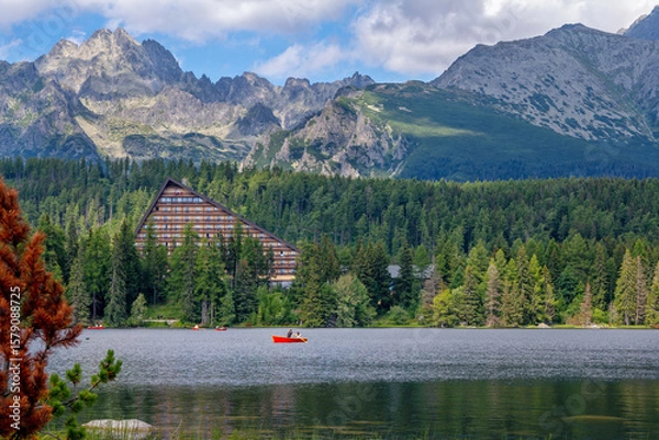 Fototapeta Scenic summer view of Strbské Pleso in the High Tatras, Slovakia. Tourists enjoy peaceful boat rides on the crystal-clear mountain lake, surrounded by a lush green forest