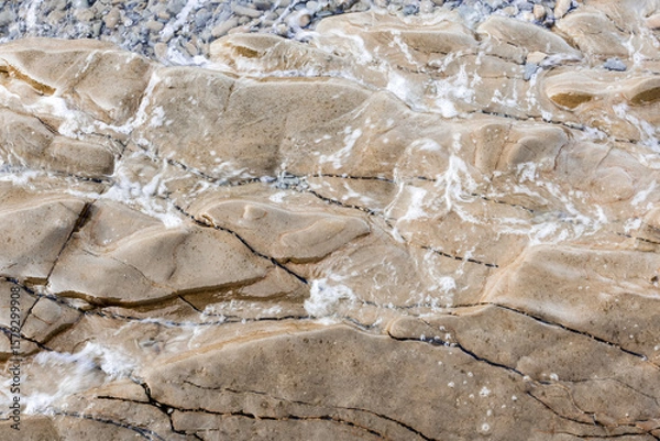 Fototapeta dynamic abstract rock formation in light beige tones under calm sea waves. abstract background with rock texture in warm tones