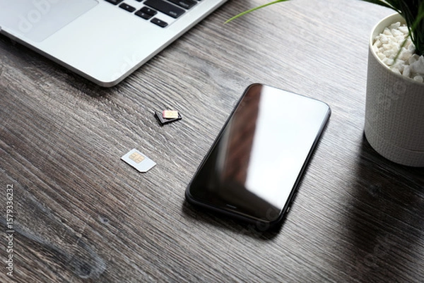 Fototapeta Two SIM cards, a modern smartphone and a laptop are lying on a wooden table.