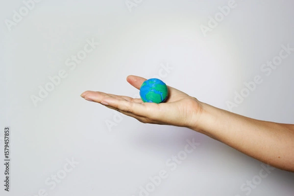 Fototapeta Hand presenting miniature Earth globe on open palm against neutral background, representing environmental care and responsibility. Environmental conservation concept. Humanitarian aid an global unity.