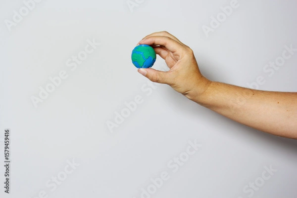 Fototapeta Single hand delicately grasping small Earth globe with fingers against neutral background, symbolizing environmental protection and care. Earth day concept. Environment day. 