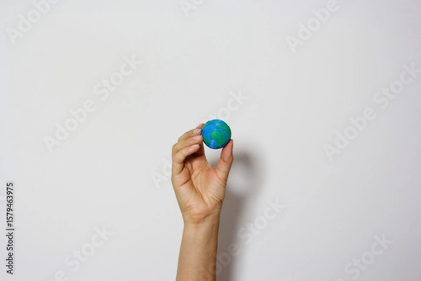 Fototapeta Single hand reaching up holding miniature Earth globe against neutral background, symbolizing environmental aspirations and global responsibility. Planet earth. Earth day concept. Save the planet