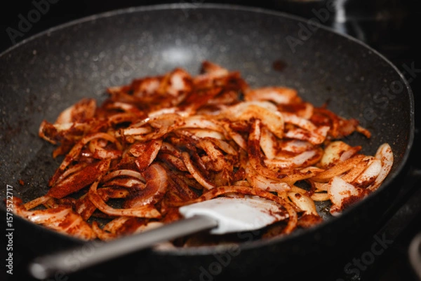 Obraz Sliced onion with paprika powder in a pan, fried on a gas stove, with a visible spatula, in natural light