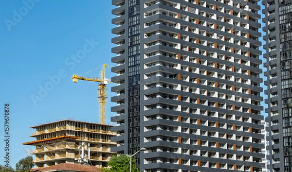 Fototapeta High-rise building and tower crane. Cityscape photograph capturing a modern building next to an under-construction structure with tower crane. idea of The architecture and ongoing development.