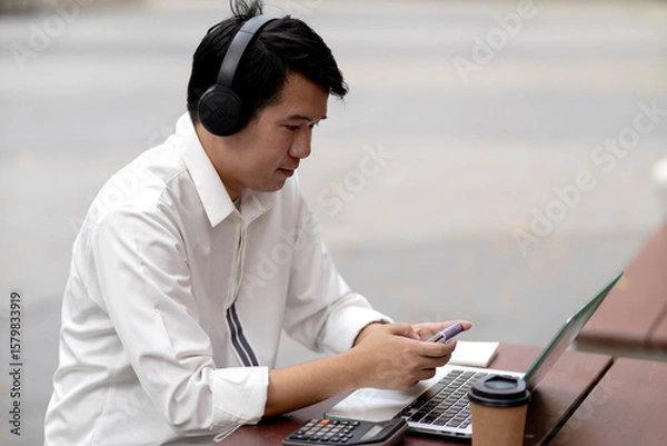 Fototapeta man wearing headphones while typing data on a laptop for communication or entertainment
