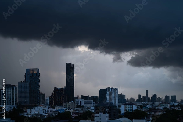 Fototapeta Dark clouds cover the sky before rain with tall buildings of city background when monsoon season.