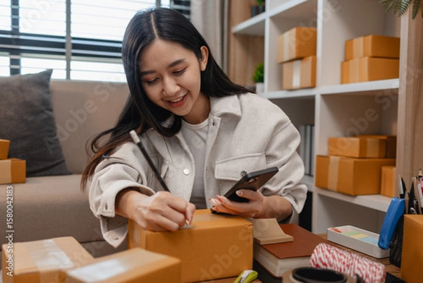 Fototapeta an entrepreneur is packing parcel for order from customer, she own a small business, sme, a lot of package in the room, e-business is running by a this entrepreneur, online shopping