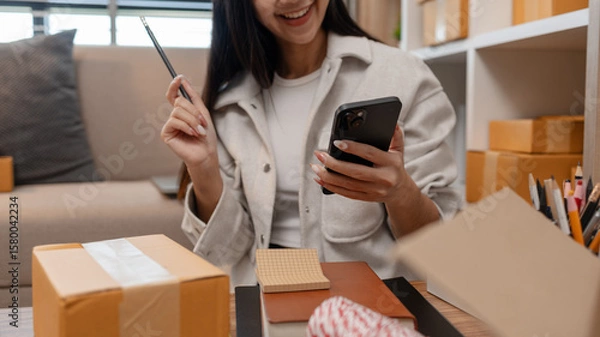 Fototapeta an entrepreneur is packing parcel for order from customer, she own a small business, sme, a lot of package in the room, e-business is running by a this entrepreneur, online shopping