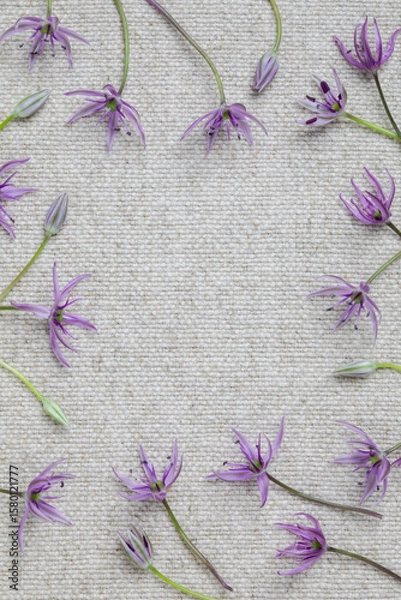 Fototapeta Flat lay of delicate purple wildflowers arranged in a circular frame on textured natural linen fabric, with space in the center for text or design or product placement