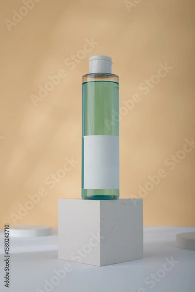 Fototapeta Transparent Cosmetics bottle with blue liquid, mockup on concrete cube stand, yellow background. Unbranded beauty container, no label template. copy space