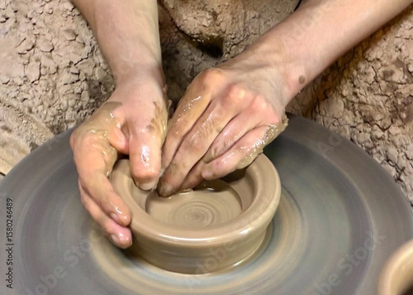 Obraz Throwing pottery on wheel. Hands of young potter working with clay and making vase or pot, jug or mug. Closeup.