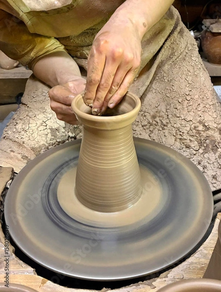 Obraz Vase made of raw clay in process of being hand-made by master, hands of young potter pulling out neck of future vase. Closeup.