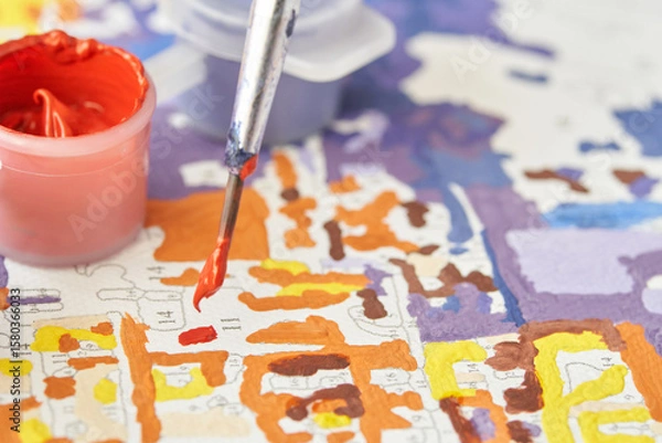 Fototapeta Close up of paintbrush and paint by numbers canvas with vibrant colors.