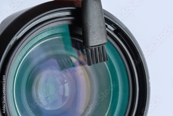 Fototapeta Close up of camera lens with cleaning brush on transparent surface with reflection.