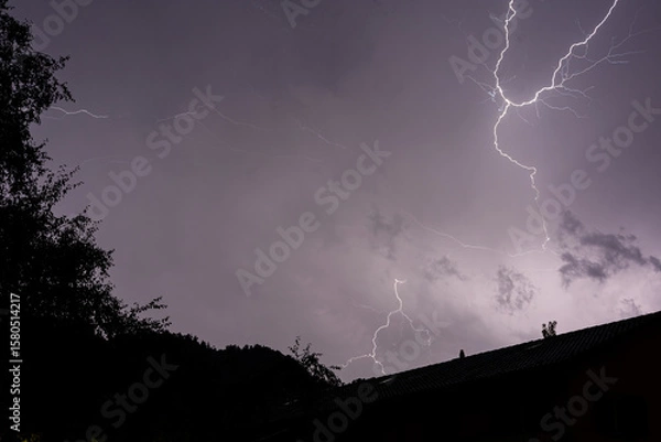 Obraz Dramatic Lightning Bolt Illuminating a Dark Sky Over a Rooftop