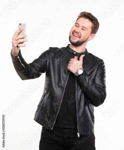 Fototapeta Man smiling while taking a selfie in a casual indoor setting with a black leather jacket