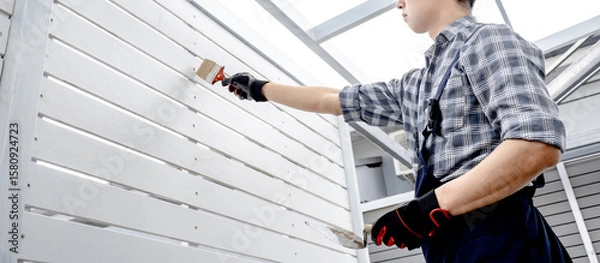 Obraz Construction worker man using paintbrush and plastering trowel for bolt head grouting on white wooden wall panel. Construction defect repair process