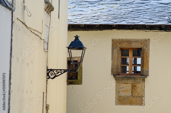 Obraz Charming close-up of an old stone window with wooden frame and classic black lantern on a rustic European house, evoking timeless village architecture.