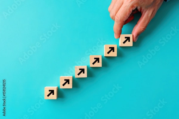 Fototapeta Hand Placing Wooden Block with Arrow on Teal Background, Symbolizing Progress, Growth, and Strategic Planning in Business and Personal Development, Achieving Goals