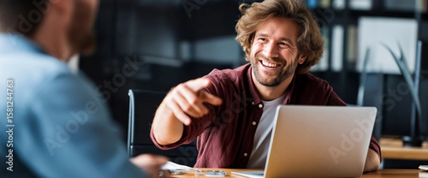 Fototapeta Cheerful Office Meeting: An enthusiastic man gestures expansively in a meeting while a laptop sits ready for action on the table, embodying collaboration in the modern workspace.