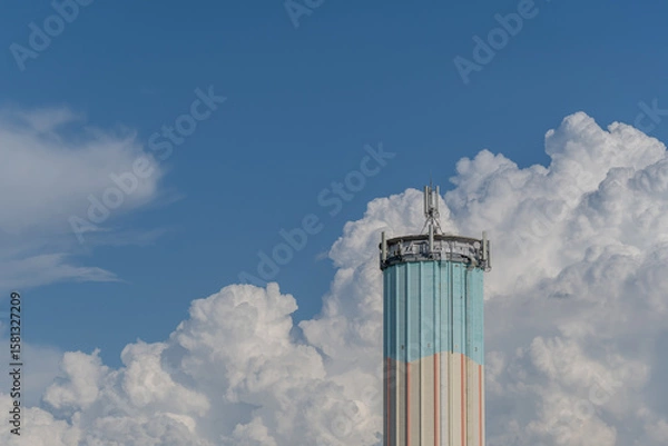 Fototapeta Bright water tower stands against dramatic clouds in a clear blue sky during a summer afternoon in a suburban area
