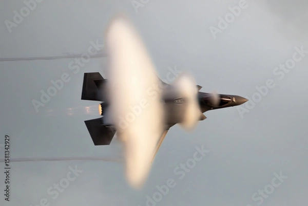 Obraz Modern fighter jet flying fast causing a vapor cone.