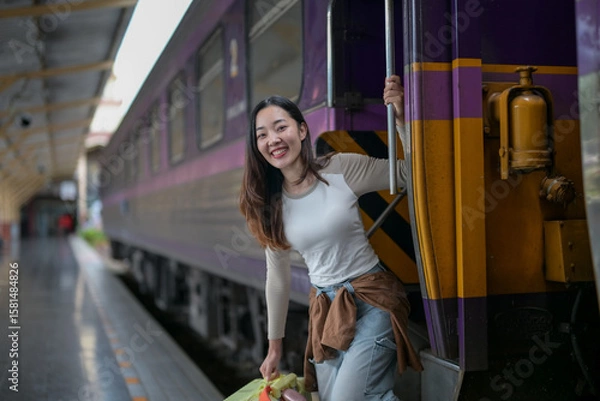 Fototapeta A woman is standing on a train platform with a green bag