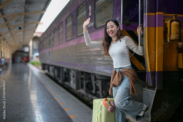 Fototapeta A woman is standing on a train platform with a suitcase