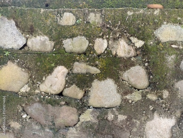 Fototapeta Mossy Stone Wall Texture. A close-up of an old wall made of various sized stones, heavily covered and joined by green moss and dirt