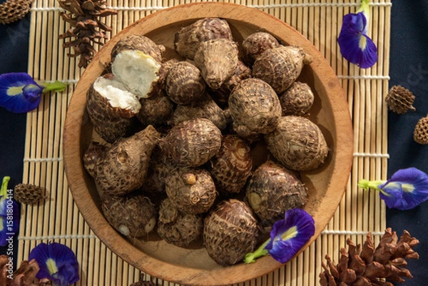 Fototapeta Organic farm‑to‑table produce in flat lay view, freshly steamed taro roots styled with blue flowers and pine cones.