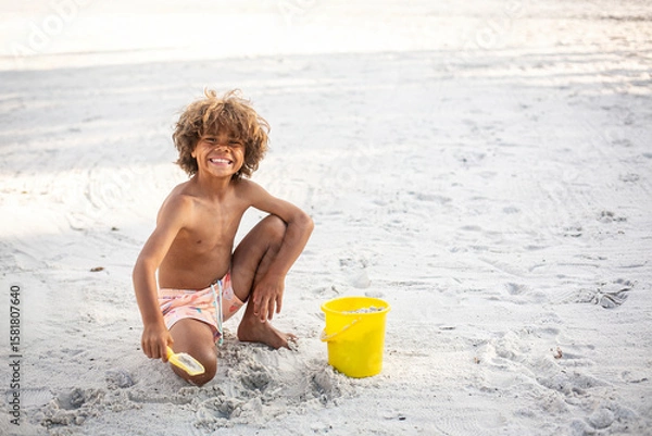 Obraz Cute diverse little boy playing in the sand at the beach while on vacation. Digging in the sand with a shovel and bucket