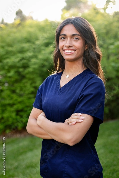 Obraz Multiethnic nursing student standing outside wearing her scrubs and looking at the camera. Attractive female medical student photo