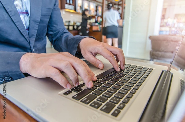 Fototapeta Close-up of business man hands on laptop keyboard. On wooden table is a smartphone .Man is shopping online. Young man surf the Internet on your computer.