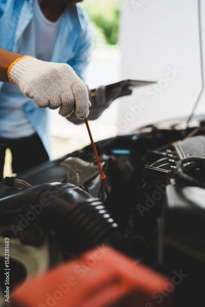 Fototapeta Mechanic wearing gloves inspecting car engine, checking engine oil with dipstick, focusing on maintenance and repair to ensure car performance, safety and efficient car care in the repair shop.