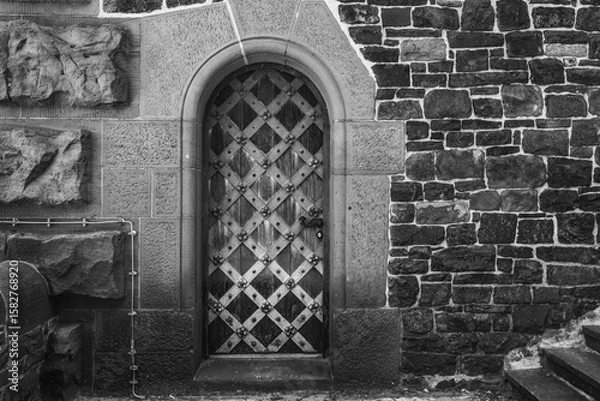 Fototapeta Rustic wooden door with diamond pattern nestled in ancient stone wall exudes timeless charm and mystery in an old town setting