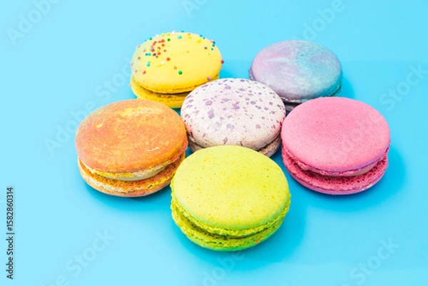 Obraz Six bright macarons laid out as a flower on a blue background. Tasty colorful macaroon assorted. Macaroons cakes of different colors. French pastry made from egg whites. Culinary and cooking concept.