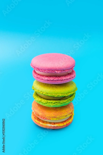 Obraz Three brightly colored stacked macarons on blue background. Mixed of colorful macaroni or pasta cake. Tasty and colorful french macarons. Culinary, cooking concept, styling food. Vertical