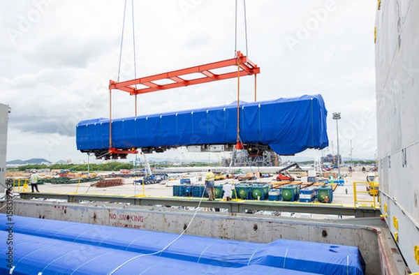 Fototapeta Unloading operation of project  cargo with port heavy lift cranes A crane on a large cargo ship docks loading a new passenger train at Laem Chabang Port