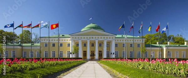 Fototapeta  Tauride Palace, Saint Petersburg, Russia. Clear blue sky, green grass, red tulips and European flags in front of Palace.