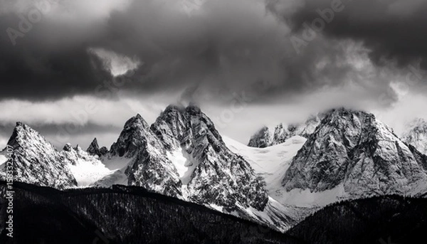 Fototapeta majestic snow covered mountain range with rugged peaks under dramatic cloudy sky in black and white