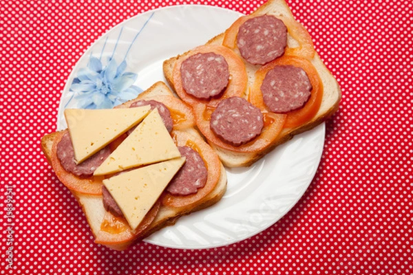 Fototapeta Toast with sausage and cheese on a plate on a red table
