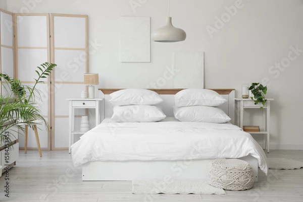Fototapeta Interior of light room with white linen on bed, folding screen and tables