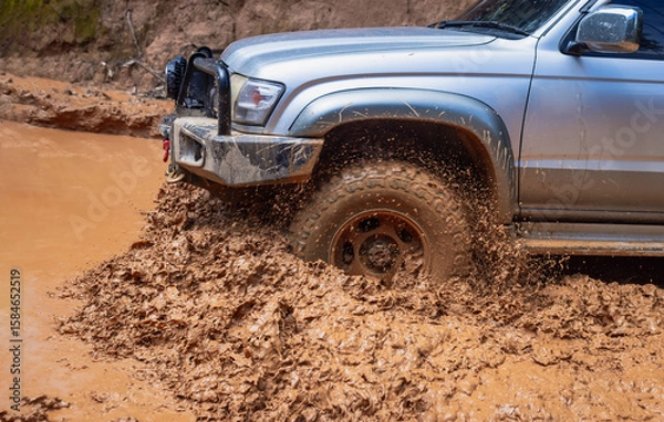 Fototapeta Off-road vehicle running on a muddy road.Close-up of an off-road vehicle tire kicking up dust and dirt on a rugged terrain.