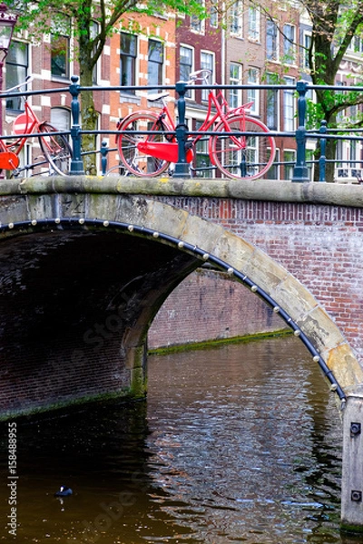 Obraz red bicycle padlocked to bridge railings in amsterdam