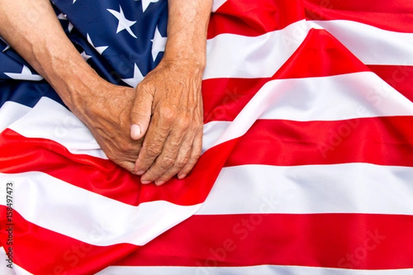 Fototapeta The older man put his hands on the us flag. The concept of caring for pensioners.