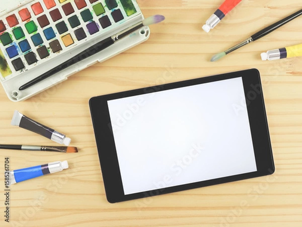 Fototapeta flat lay of artist workspace with digital tablet. Drawing tools, stationary supplies, Watercolor paints, brushes and white blank screen of digital tablet on wooden table, copy space.